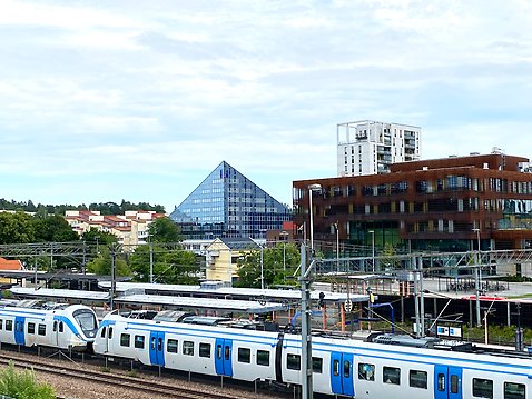 Vy över Väsbys stationsområde med pendeltåg i förgrunden och byggnader i bakgrunden.