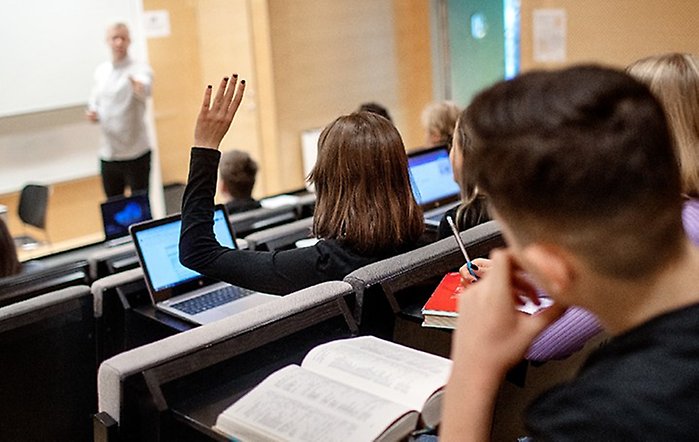 En person räcker upp handen i en föreläsningssal.