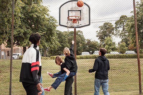 Några ungdomar spelar basket utomhus.