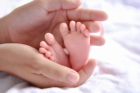 Två händer håller om två små bebisfötter 