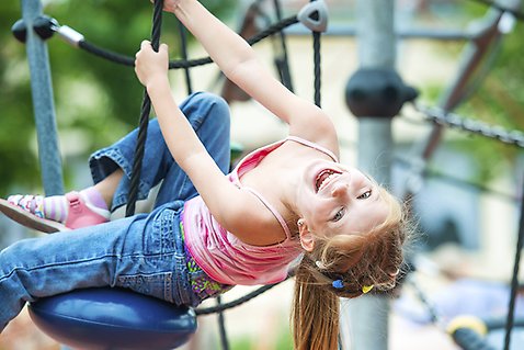 En flicka leker i en klätterställning på lekplats.